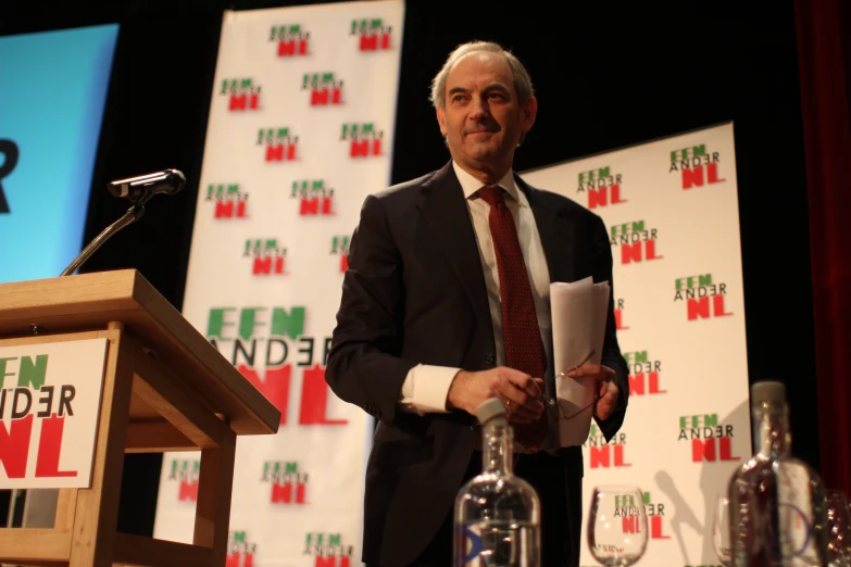 man in a suit standing behind a podium holding papers