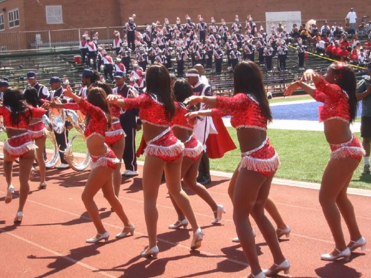 several cheerleaders are marching down the track as an audience watches