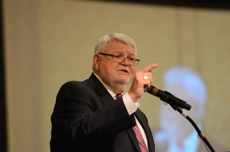 an older man in suit and tie giving a speech