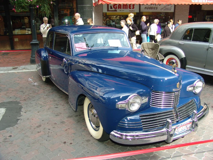 an old fashion blue car sits parked on the side of the street