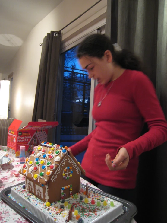 a woman in red shirt looking at a gingerbread house