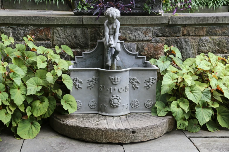 a grey water fountain on bricked path with stone planter next to it