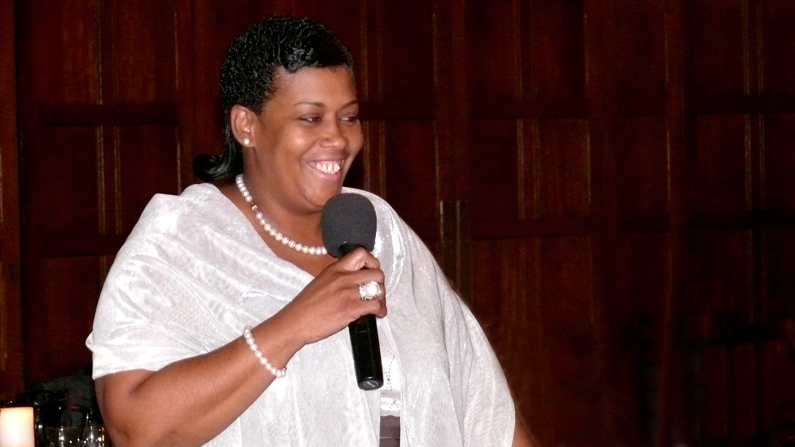 a woman in a white robe and pearls is holding a microphone