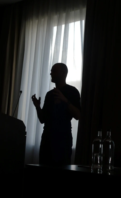 a silhouette of a man in front of curtains looking out at a window