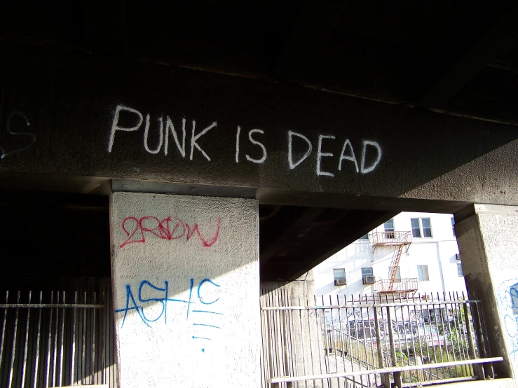 graffiti on a building reads punk is dead under an overpass