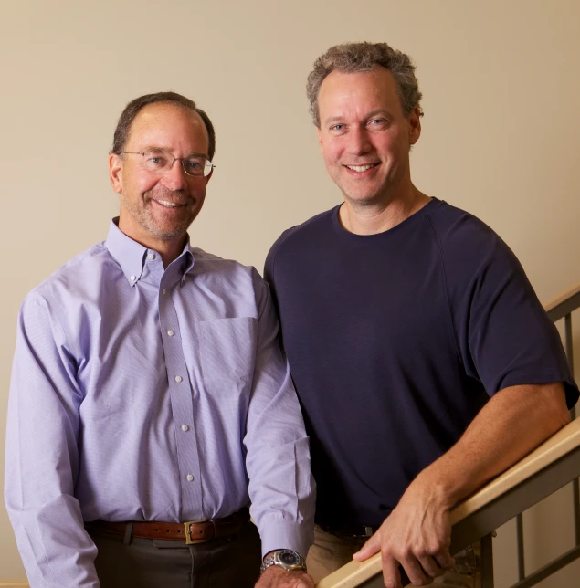 two men posing for a picture, one is holding a cane and the other a on down shirt