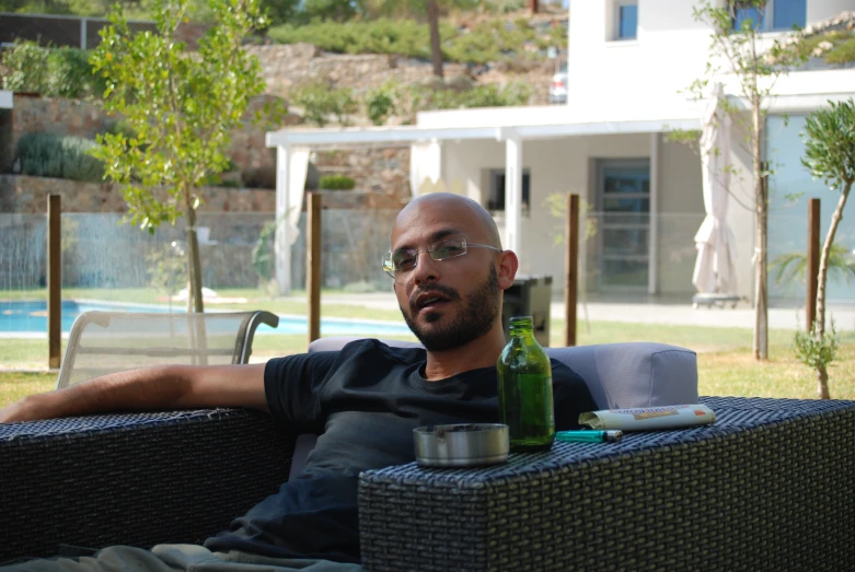 a man wearing glasses with a bottle and a toothbrush on a patio