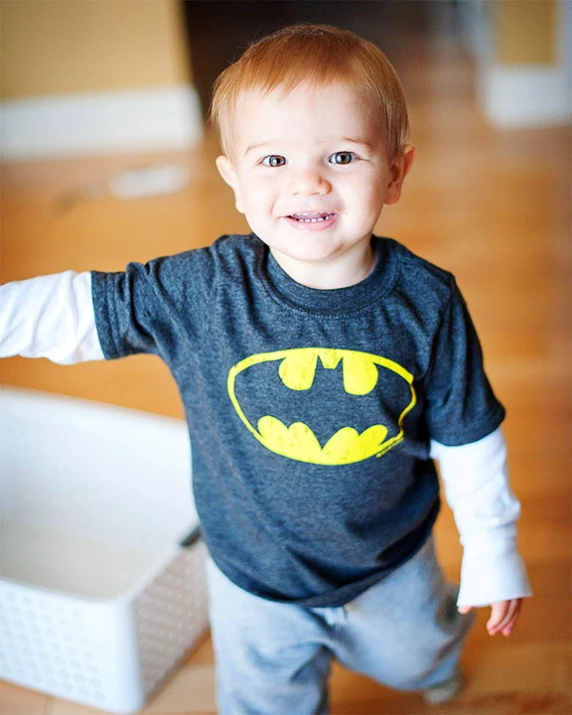 a toddler in a batman tee standing in front of a white box