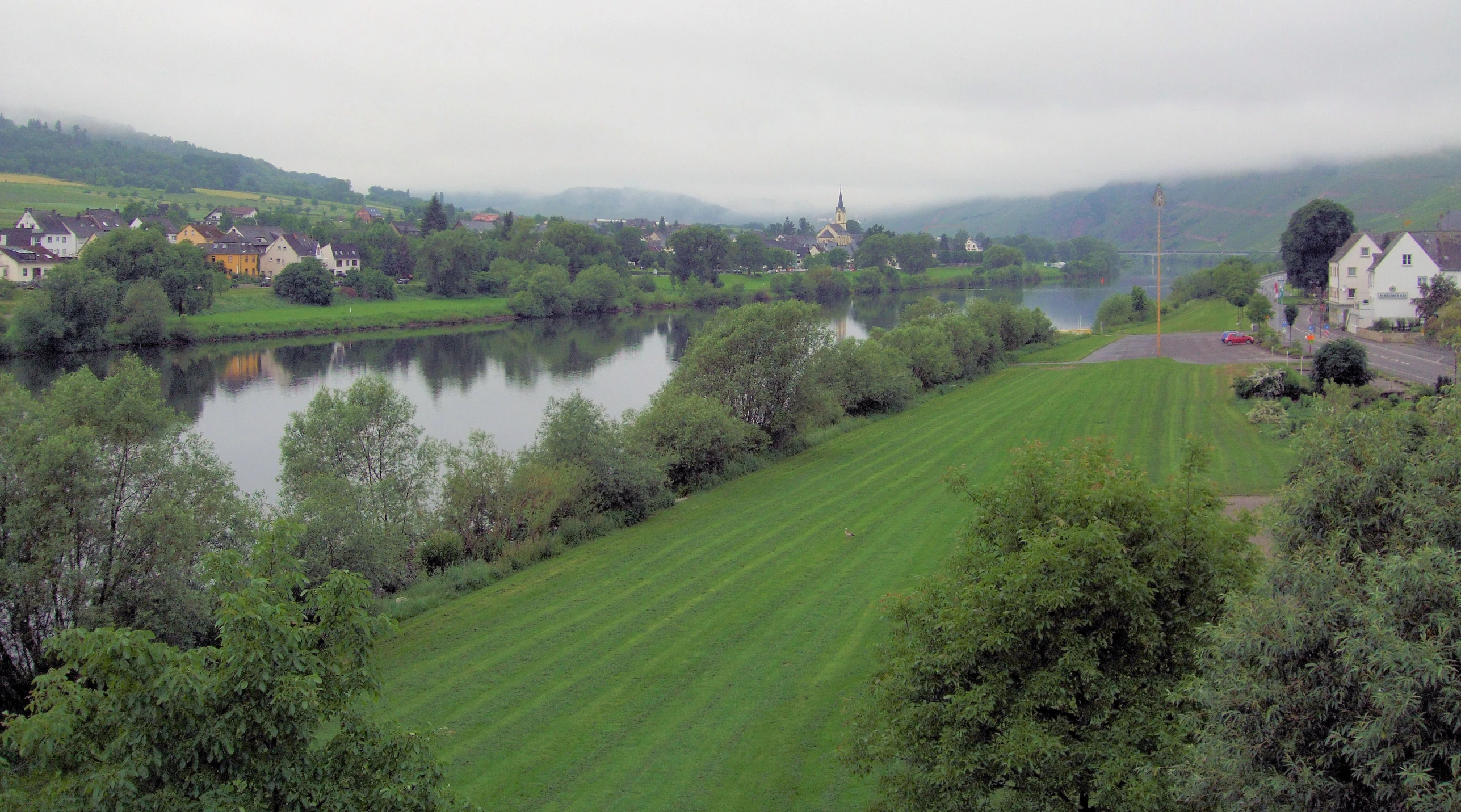 a green field in front of a river in a green valley