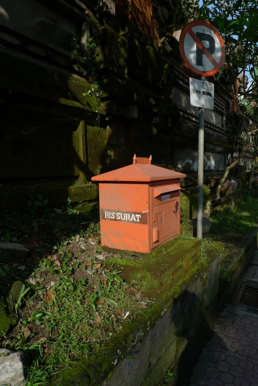 a red mailbox is in the grass near a sign