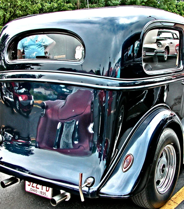 the back end of an old black car parked in a parking lot