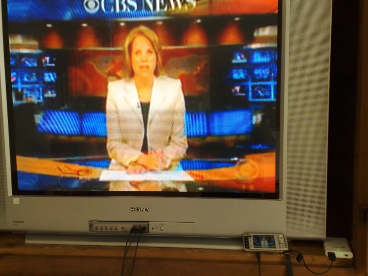 television screen displaying news with reporter sitting in chair behind