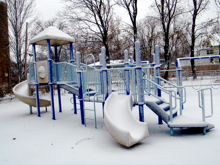 a snowy playground in a neighborhood park, with play equipment and trees