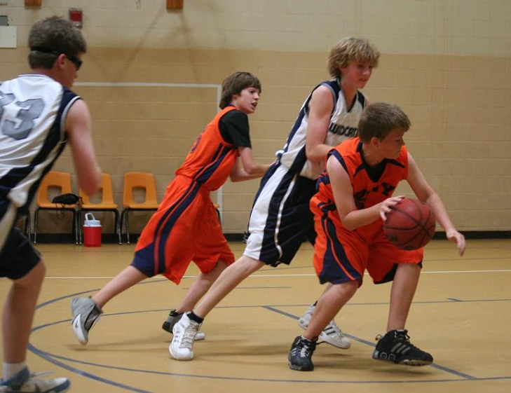 s play basketball in a gym while wearing orange and black jerseys