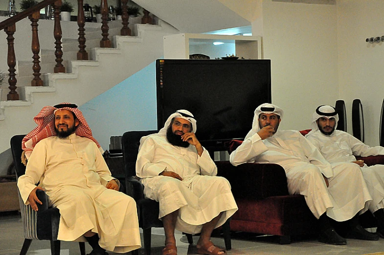 four men sitting on chairs in a building