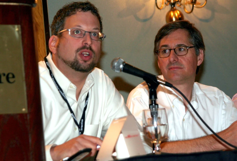 two men sitting side by side in front of a microphone