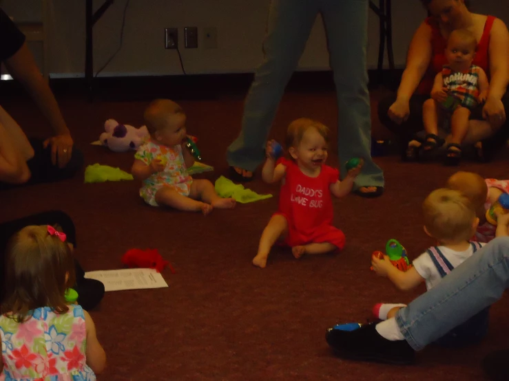 several little girls and two babies sitting on the ground in front of someone's feet