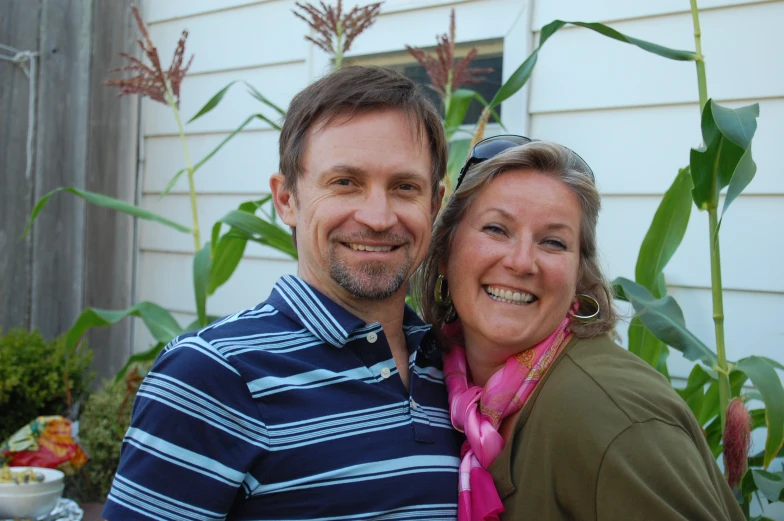 the man and woman are standing in front of a house with plant life