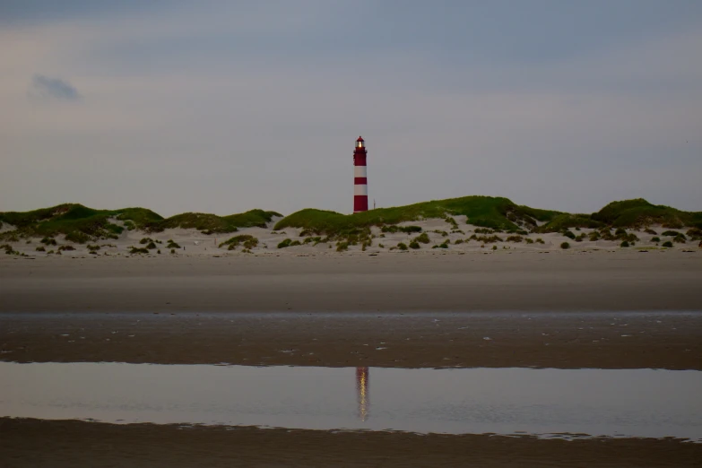 a lighthouse is located on the sand beside a body of water