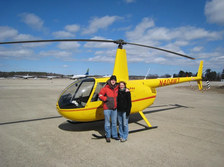 a couple posing in front of a helicopter on an airport runway