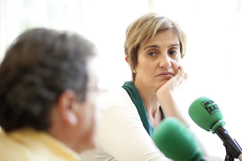 a woman sitting in front of a microphone with a person looking at her