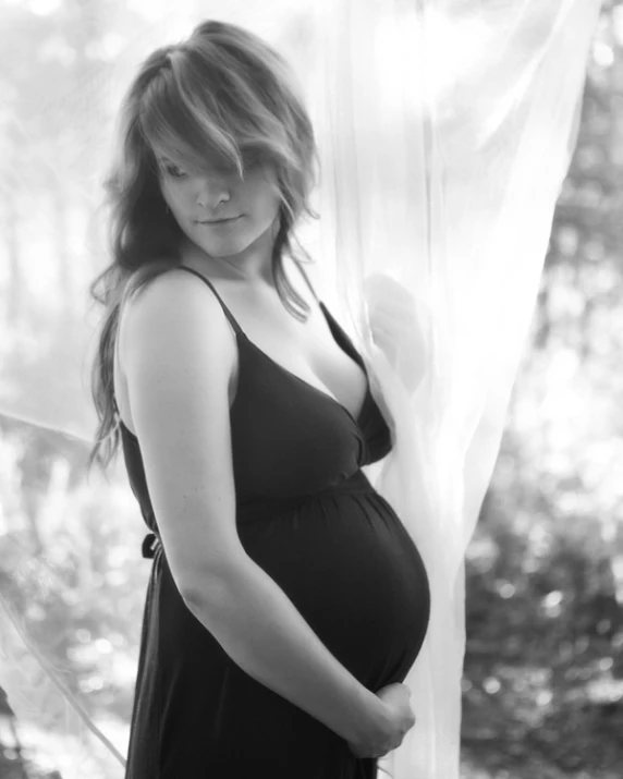 a pregnant woman leaning against the curtain in the sun