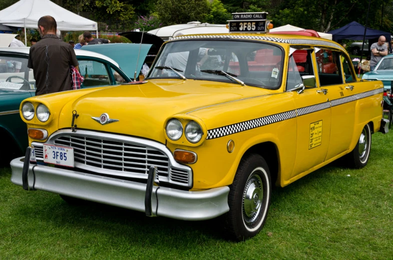 a taxi car parked next to other automobiles on a field