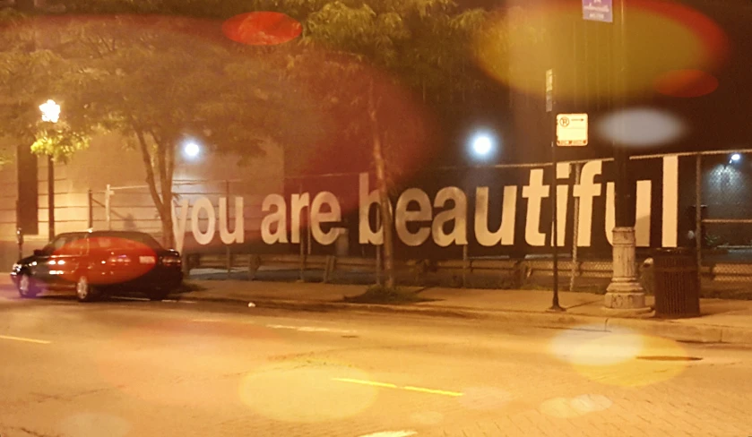 a red car parked in front of a sign reading you are beautiful