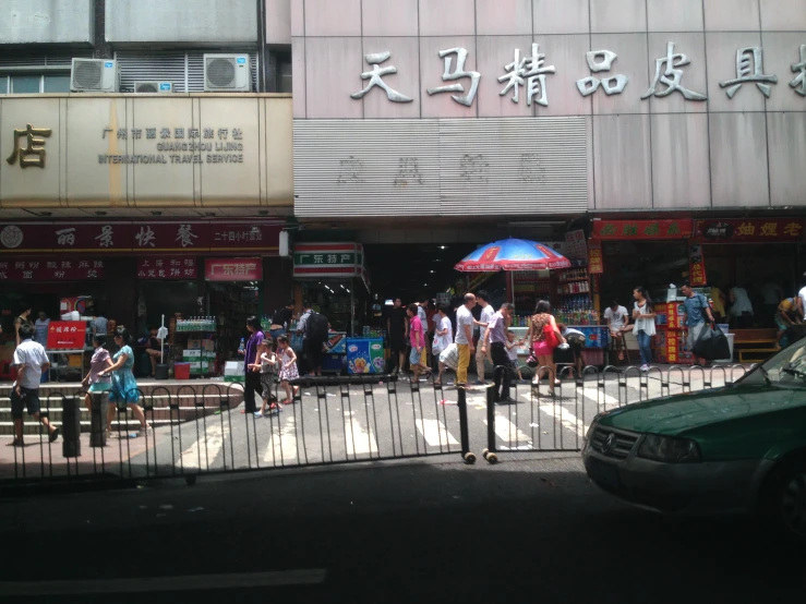 people walking on the street next to a fence and a taxi