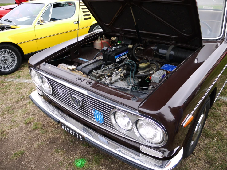 an older car with its hood open and some cars parked around it