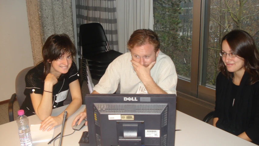 two women and one man sitting at a table looking at a computer