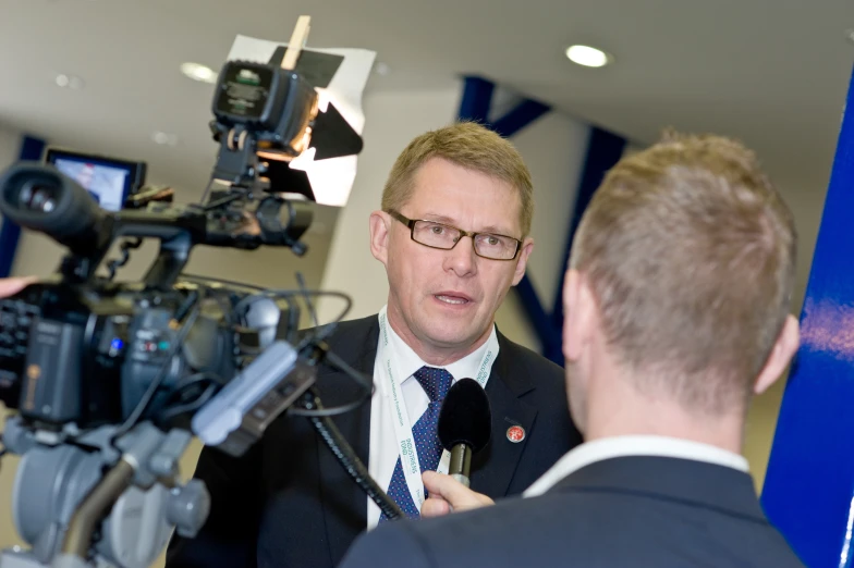 a man talking to another person in a room with film equipment