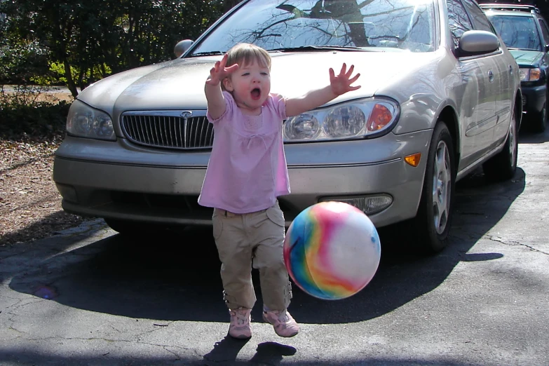  standing near a parked car and holding a ball in front of her