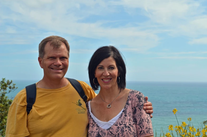 a man and woman smiling next to a bright blue ocean