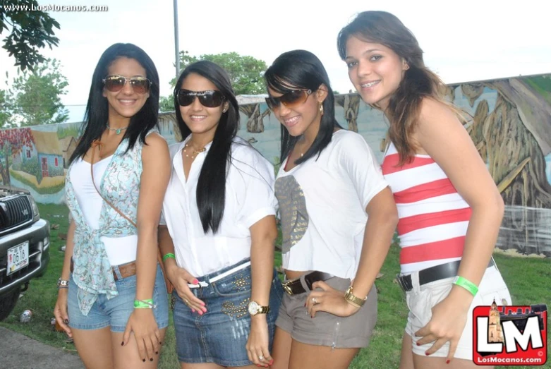 four girls posing for a po with an old car in the background