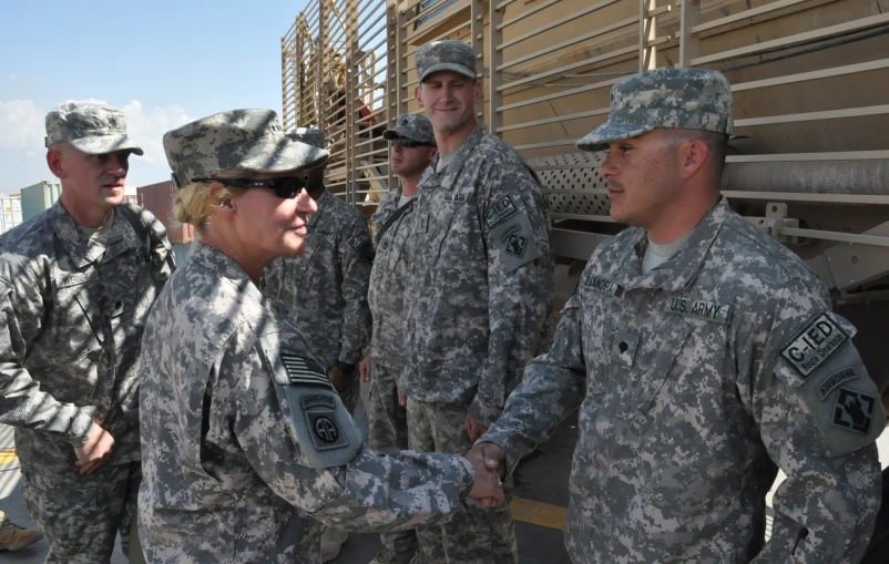 two woman shaking hands over another person in uniform