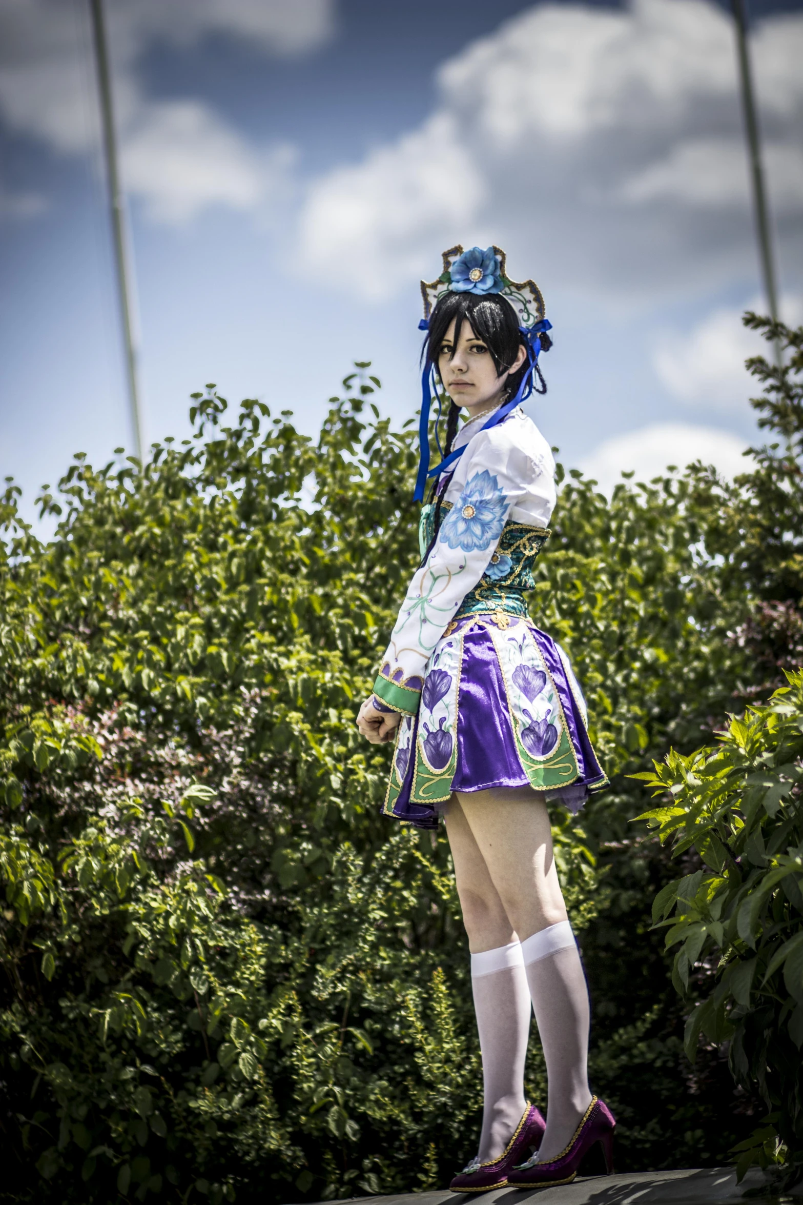 a woman with blue hair and blue eyes stands on a ledge with her hand behind her head