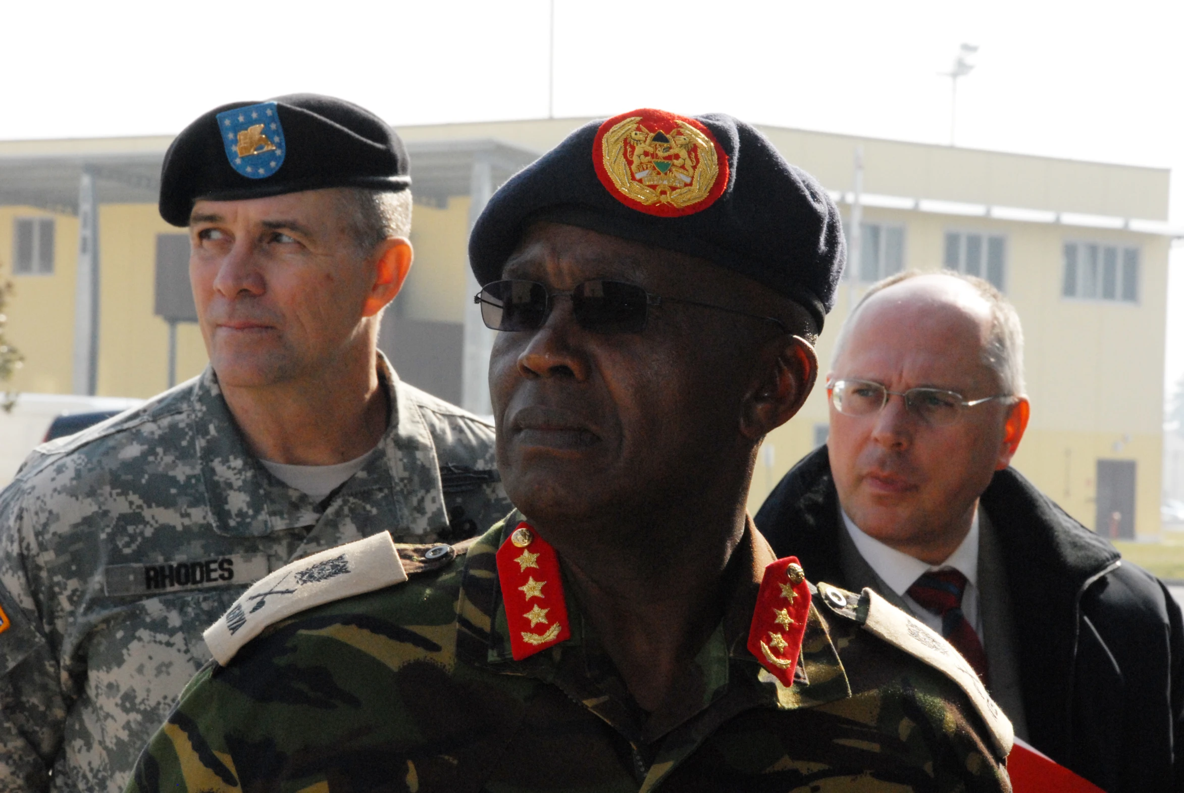 three soldiers in uniform walking past men in suits