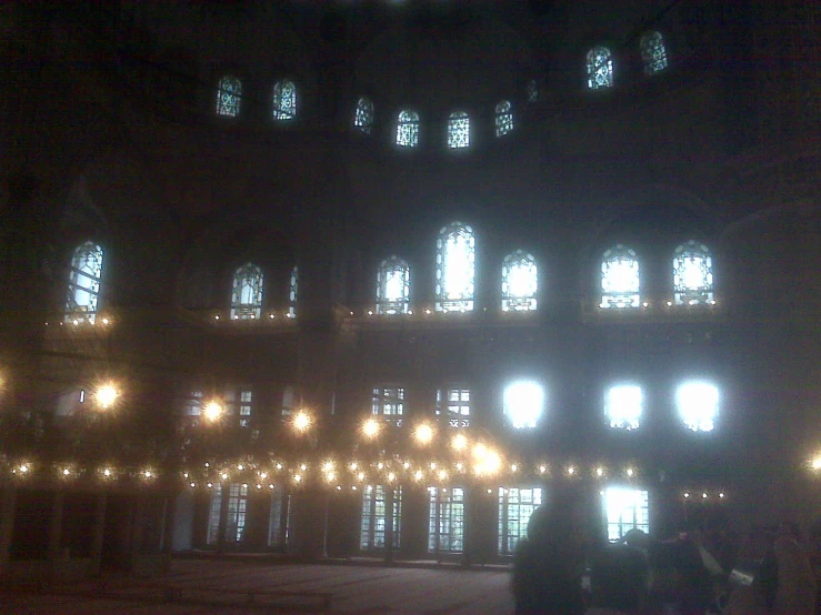 people standing around in the dark looking at a building with lights on it