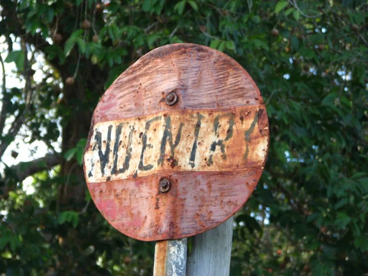 an old rusted sign is hanging on a wooden pole