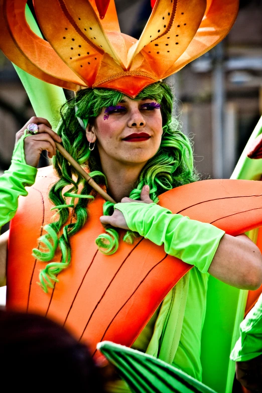 a woman in a green outfit wearing orange feathers and holding an umbrella