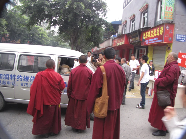 many people with long red robes are walking near a white van