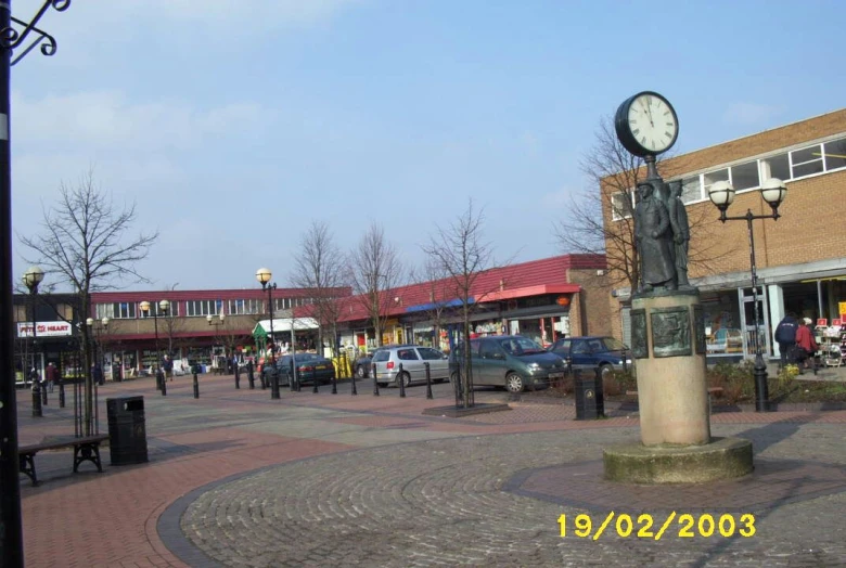 some people a clock and some buildings on a sidewalk