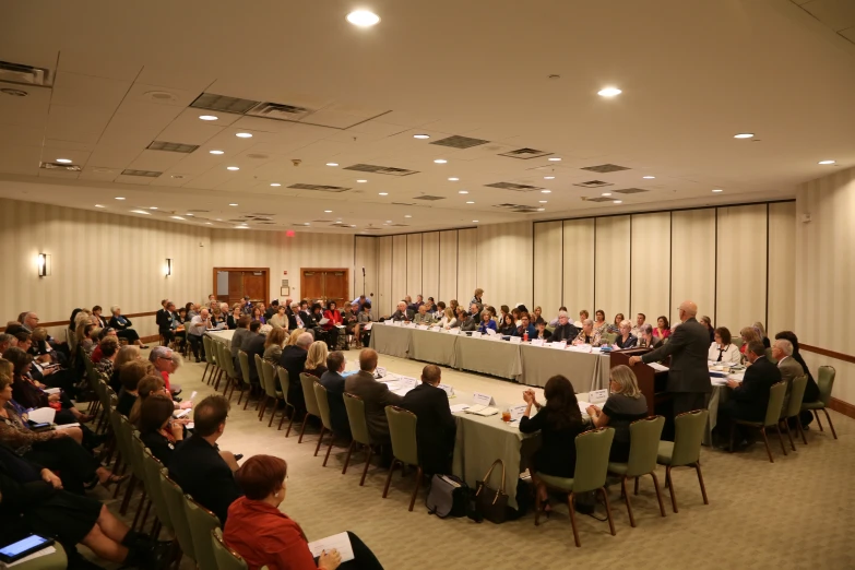 people sitting at tables in a conference hall and listening to a speaker