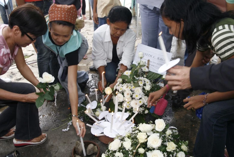 people gather around and place flowers in a vase