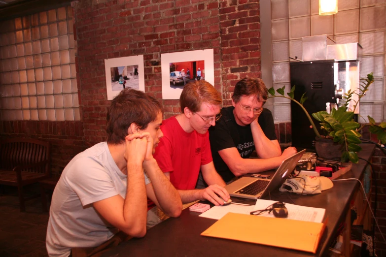 three guys are sitting at a table using a laptop