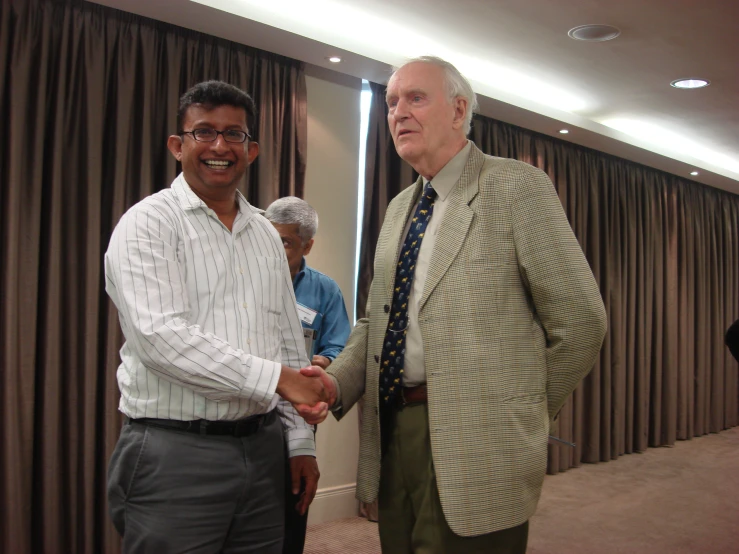 a man shaking hands with another person standing near by