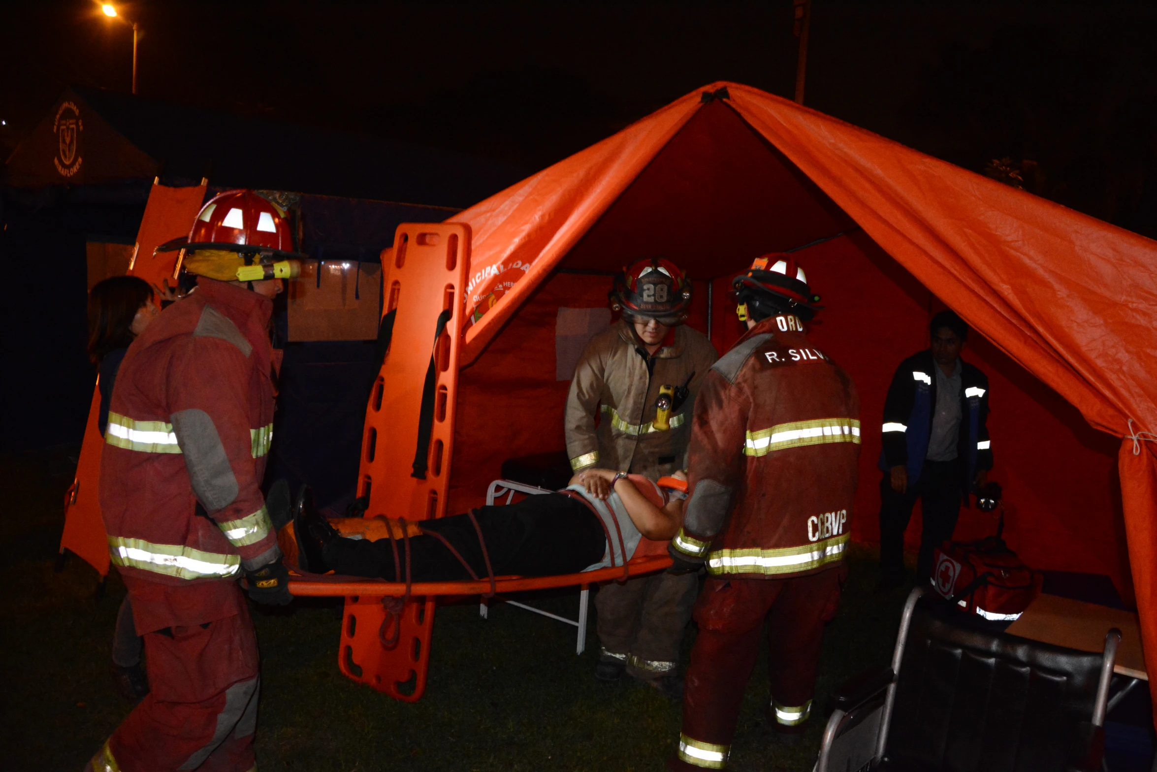 two fire fighters holding an injured person in a red tent