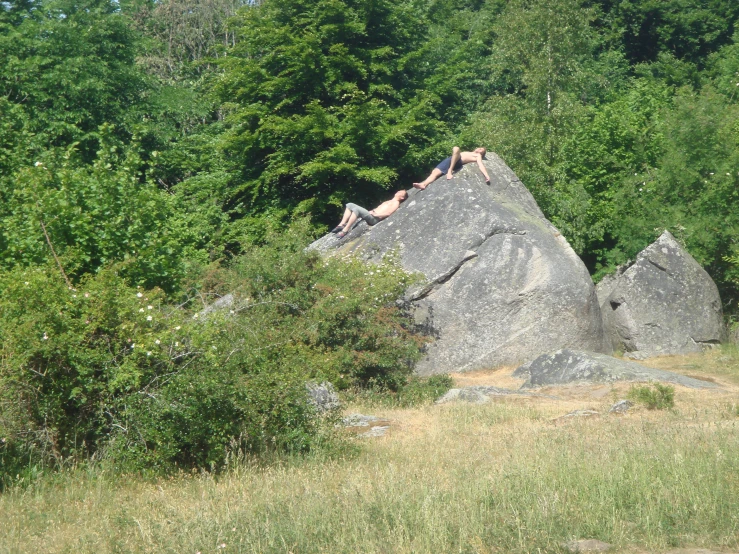 several people on the side of a hill laying on top of a rock