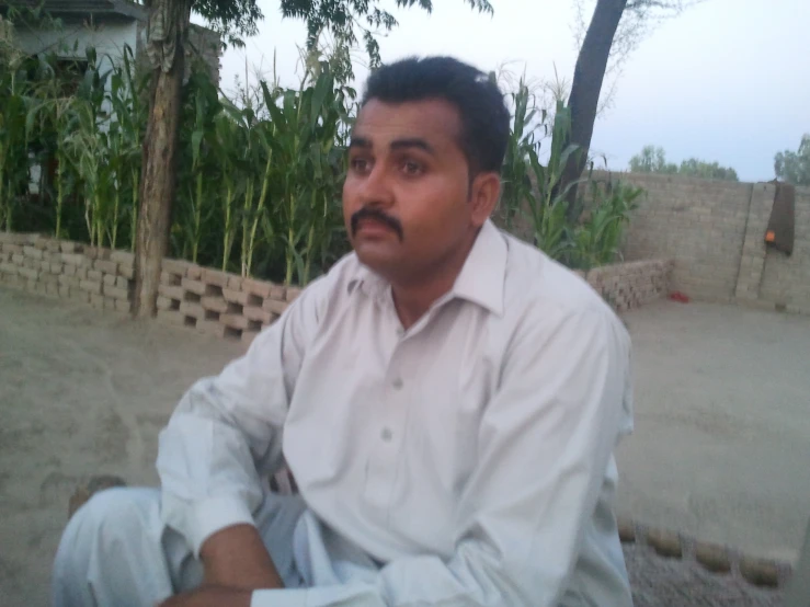 an indian man sitting outdoors near some plants